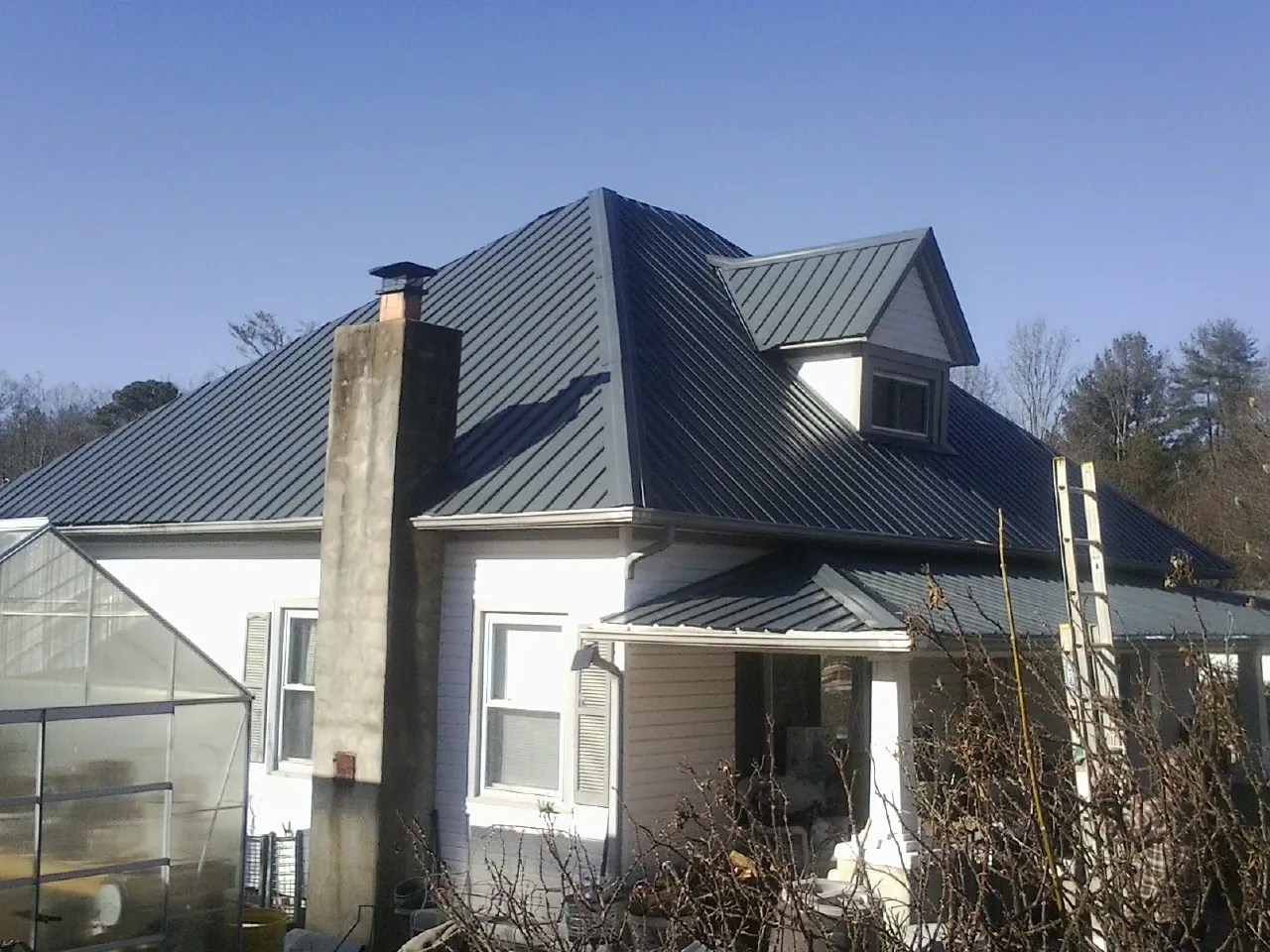 Dark blue standing seam metal roof on a white farmhouse with dormer — Slate & Tile Roof Repair by Roofing Brothers in North Creek