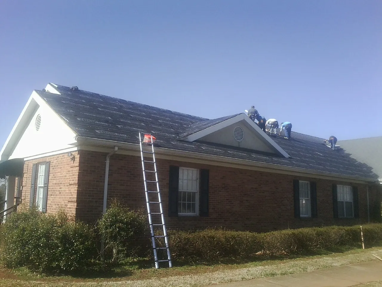 Crew tearing shingles off a brick ranch roof with a ladder set — Emergency Roof Repair work by our crew in North Creek