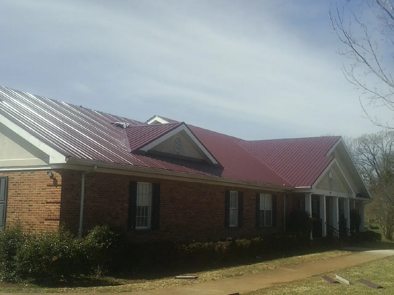 Red metal roof with gabled entries on a long brick building, from a Hail Damage Roof Repair job in North Creek
