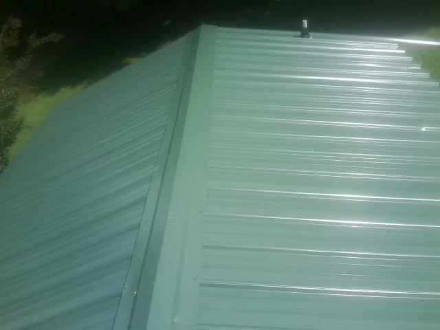 New green metal panels meeting at the ridge of a roof — Flat Roof Repair work by our crew in North Creek