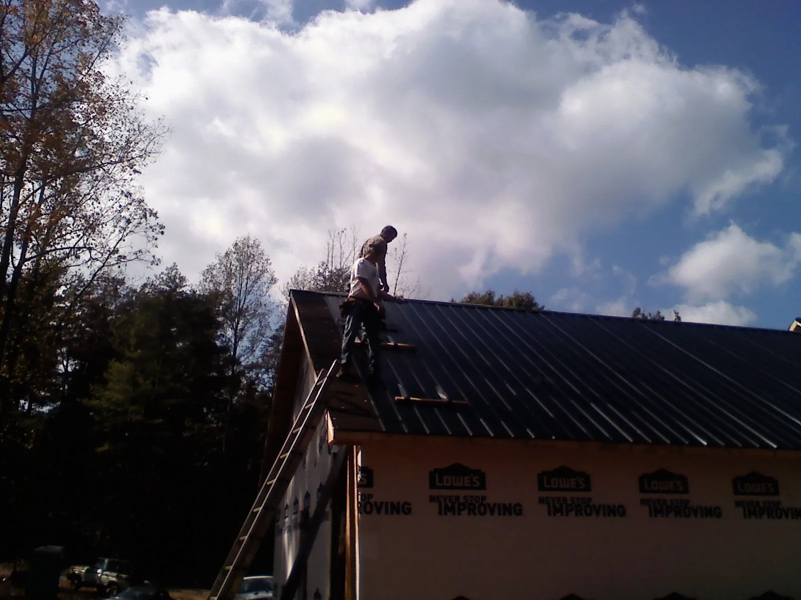Roofer fastening dark metal panels high against a cloudy sky, from a Roof Inspection job in North Creek