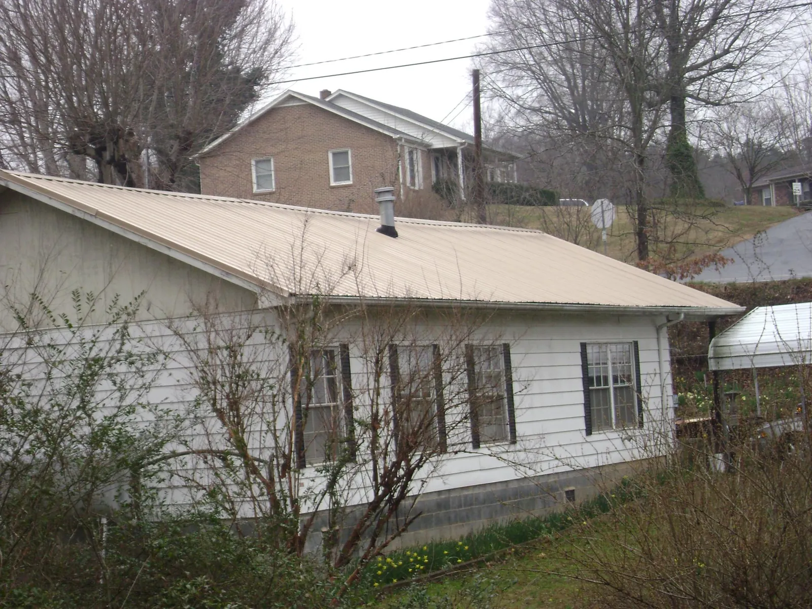 Tan metal roof on a white sided house set into a hillside — Commercial Roofing by Roofing Brothers in North Creek
